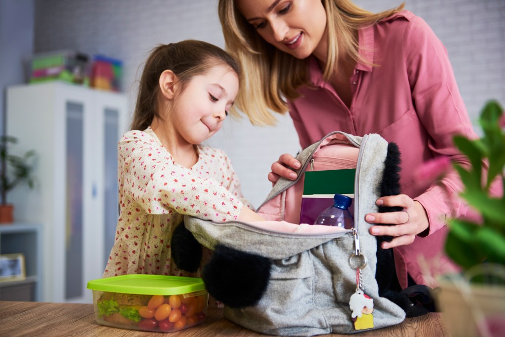 Young mom and daughter packing backpack for the school
