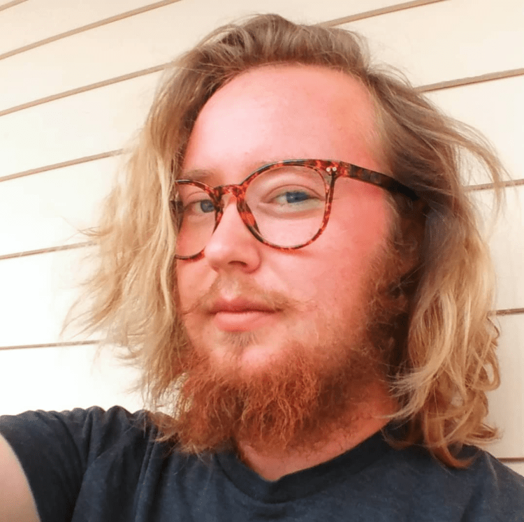 photo of finnigan white person with chin length wavy blond hair and orange beard - wearing turtle shell glasses