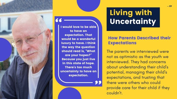 An old man setting in front of a house. The man is wearing glasses, a white t-shirt, and a drack blue jacket. The man has a white beard and white hair.