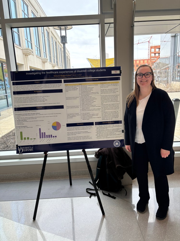 A white woman in a suit standing next to a poster.