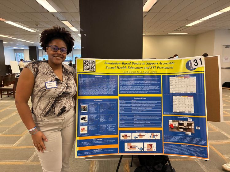 A Black woman stands next to a poster. 